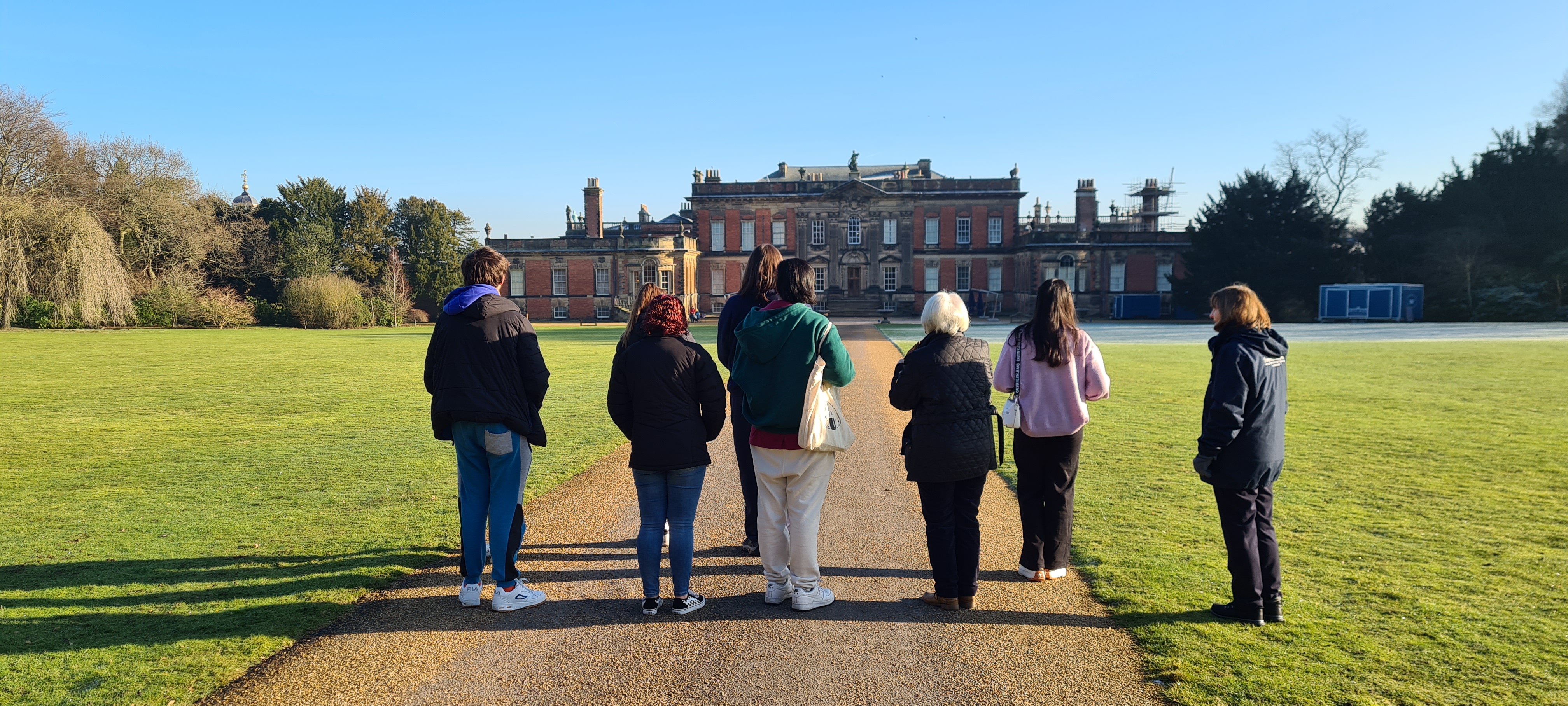 A group of young people stand outside Wentworth Woodhouse, facing the facade, on a sunny day.