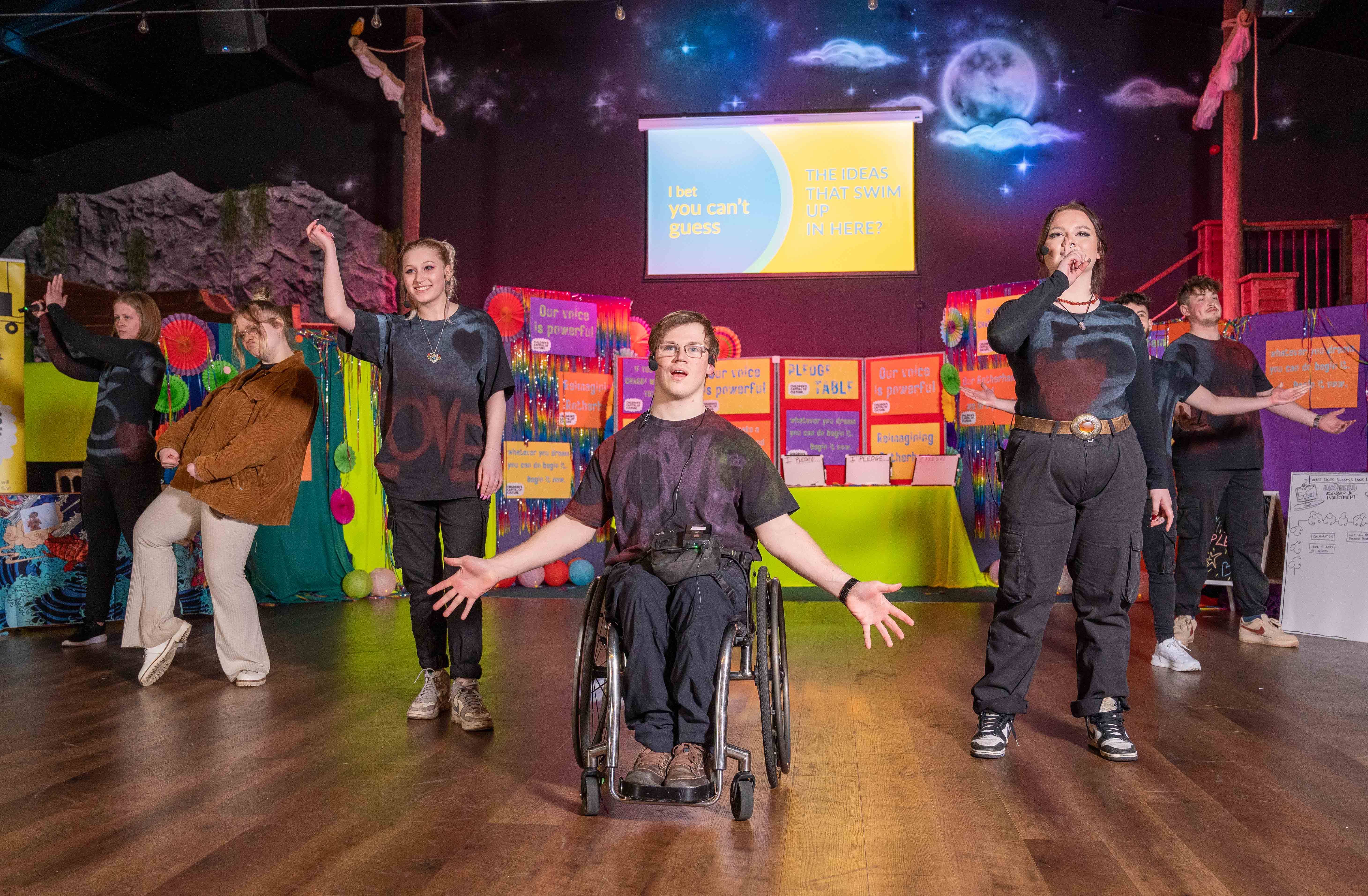 A photograph of seven young people on stage in the middle of a performance.