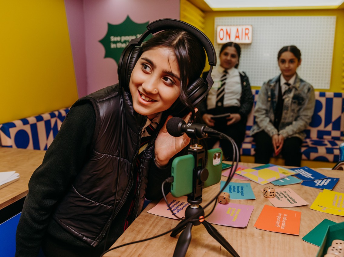 A girl heading headphones smiles for the camera.