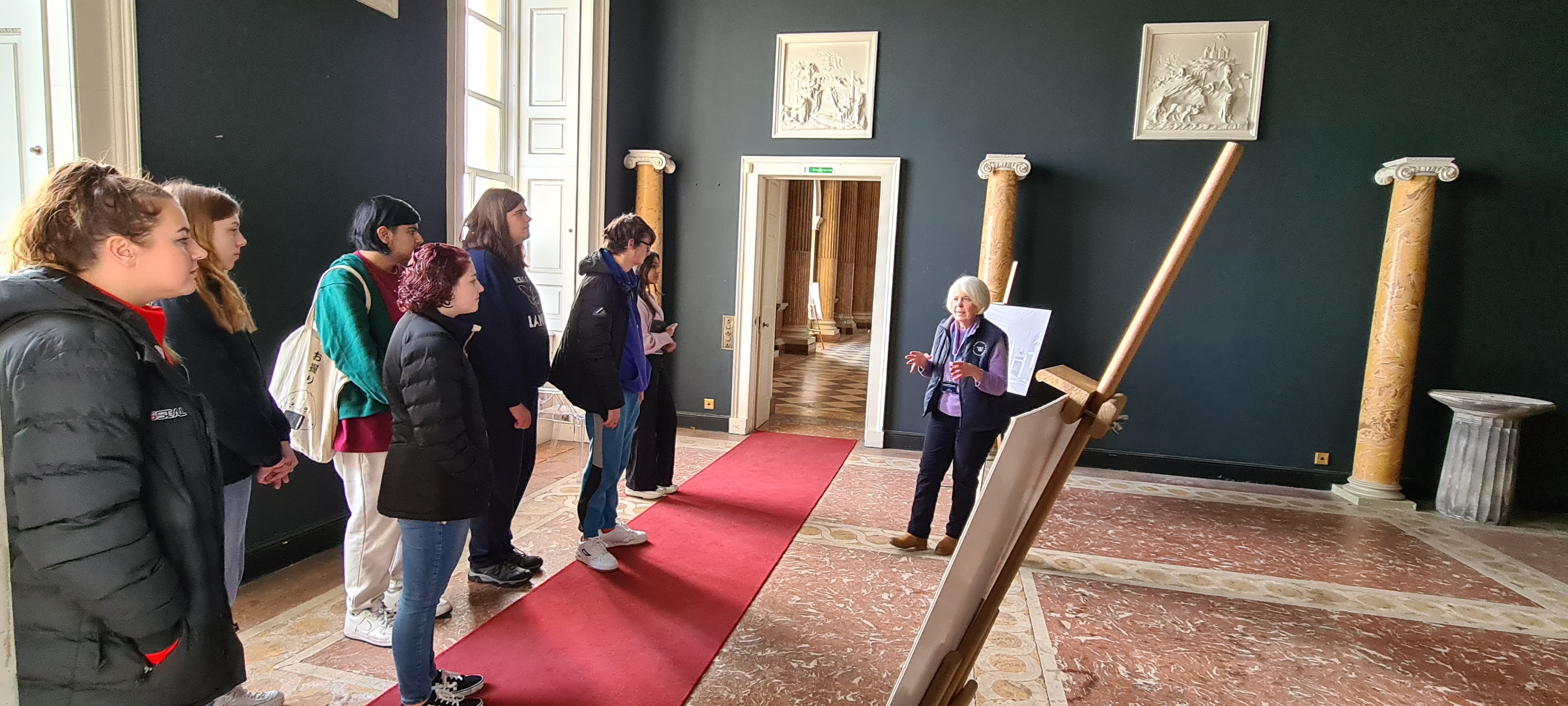 A group of young people stand inside Wentworth Woodhouse's room, led by a tour guide.